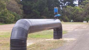 A silver Bermad pipe above ground, next to a road.